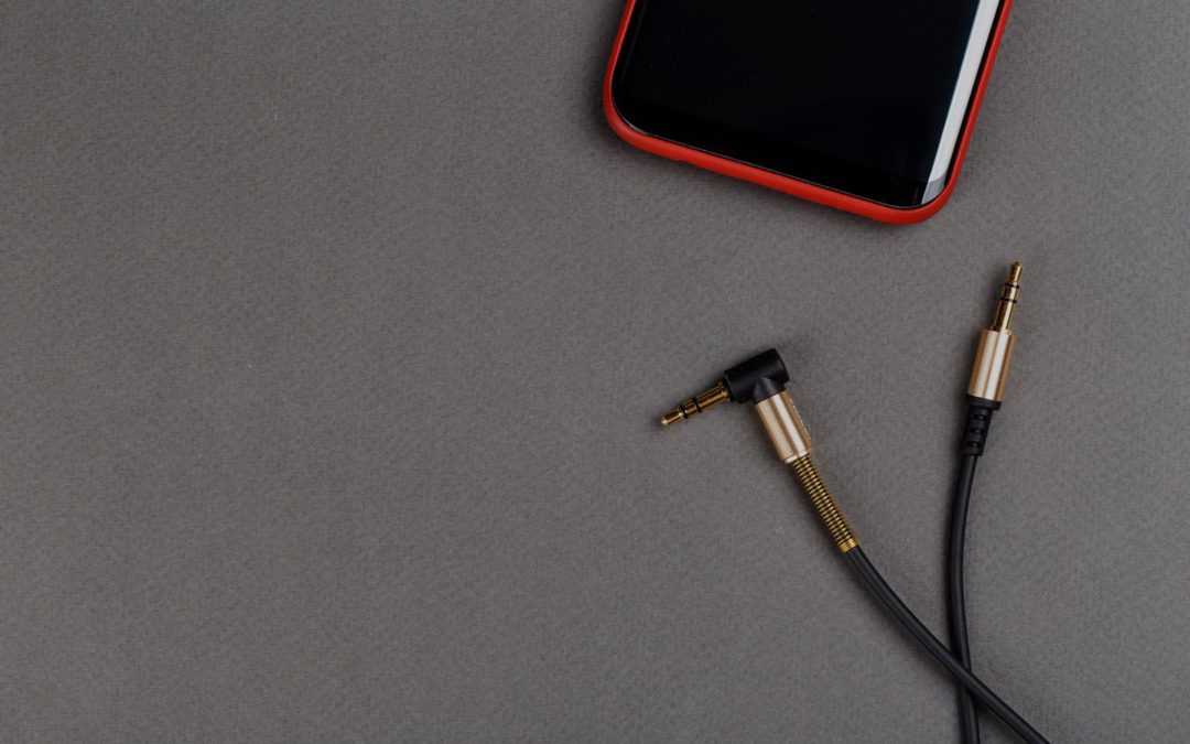 A smartphone in a red case and an auxiliary audio cable resting on grey fabric